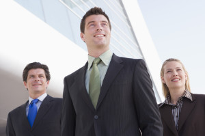 Three businesspeople standing outdoors by building smiling